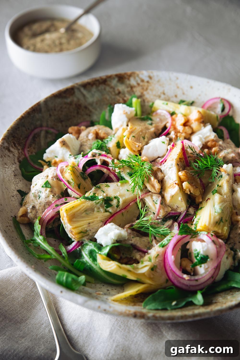 Artichoke salad with goat cheese and a lime yoghurt dressing in a ceramic bowl.