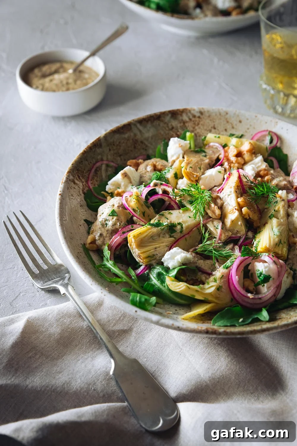A table setting with a bowl of artichoke salad and yoghurt dressing in the background.