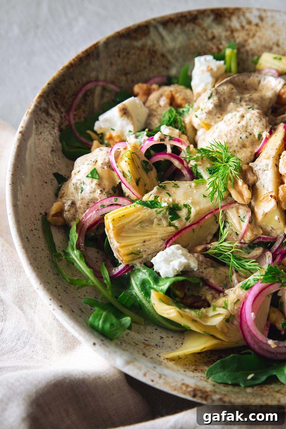Close-up of artichoke salad with goat's cheese and fresh herbs in a ceramic bowl.