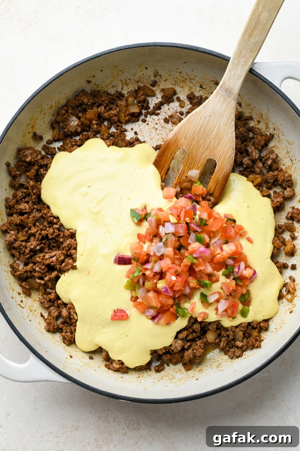 How to make Dairy Free Queso Fundido with Ground Beef: Cooked ground beef and onion in skillet with spices mixed in, cashew queso and pico de gallo on top. 