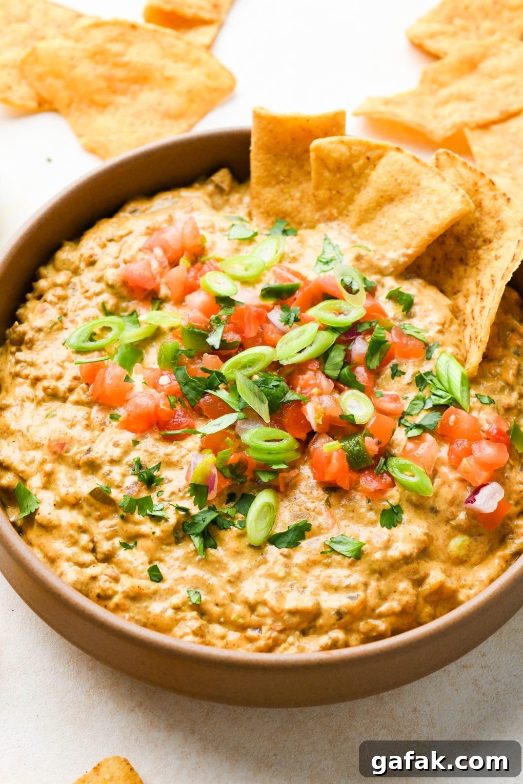 A large ceramic bowl filled with dairy free queso fundido with ground beef, topped with pico de gallo, cilantro, and thinly sliced green onions with some chips dipping into the dip.