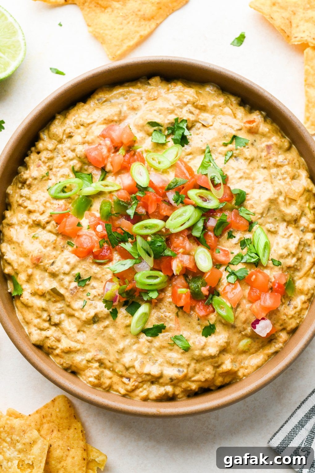 A large ceramic bowl filled with dairy free queso fundido with ground beef, topped with pico de gallo, cilantro, and thinly sliced green onions with some chips dipping into the dip.