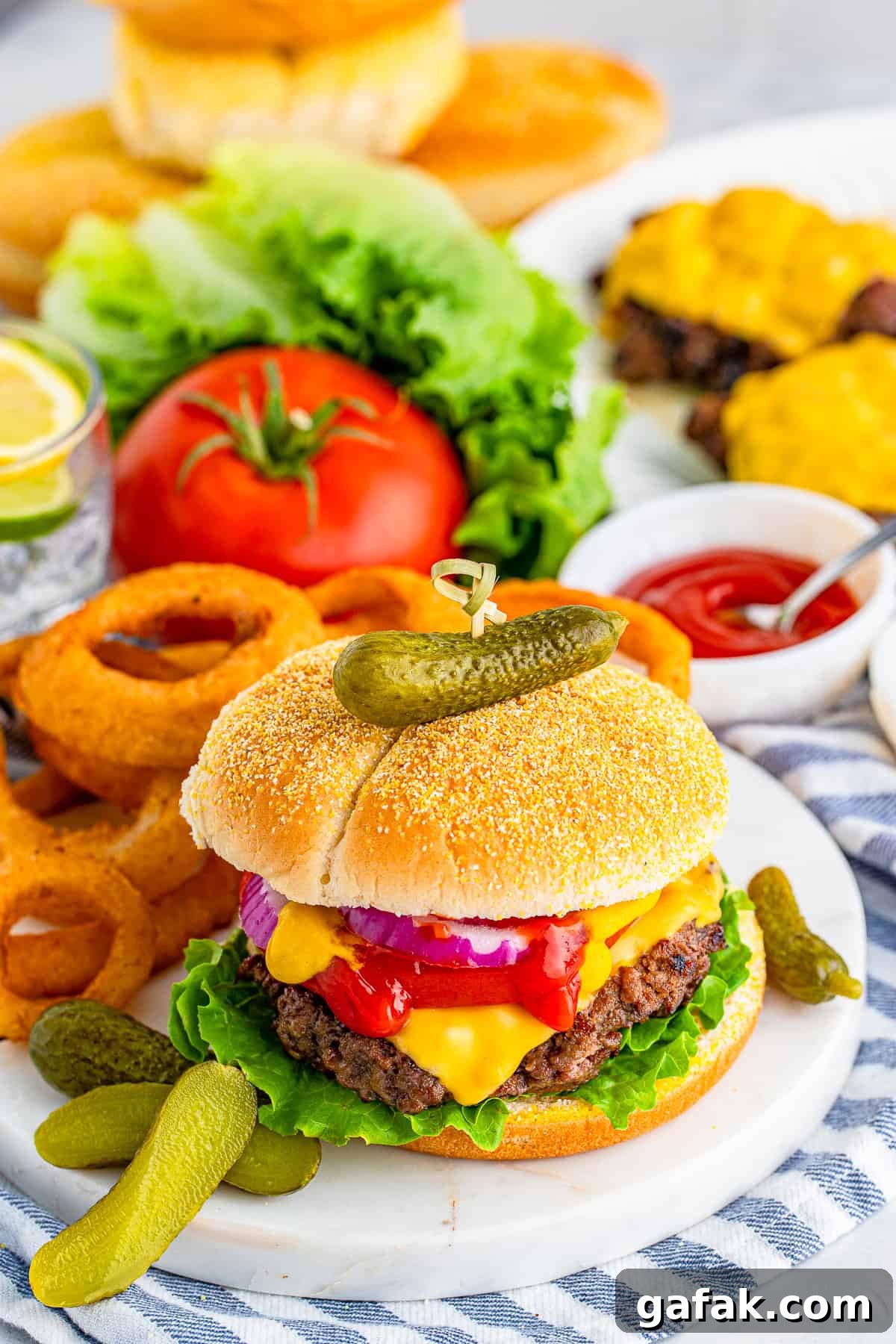 Cheeseburger on marble board with onion rings, pickles and more burgers and buns in background
