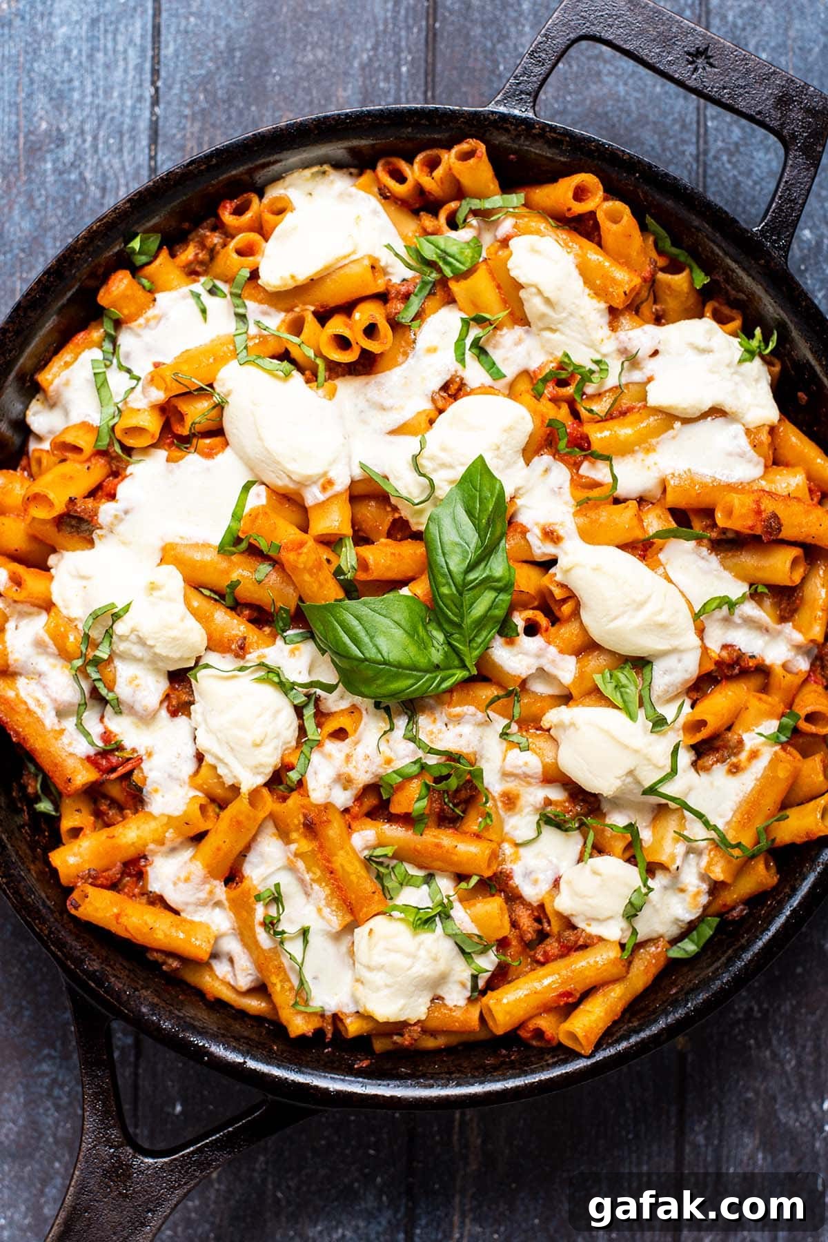 Baked ziti in a cast iron skillet topped with fresh melted mozzarella and ricotta cheese.