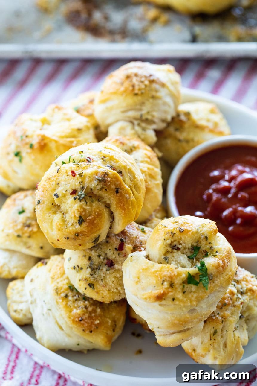 Garlic Knots stacked on a plate with pizza sauce.