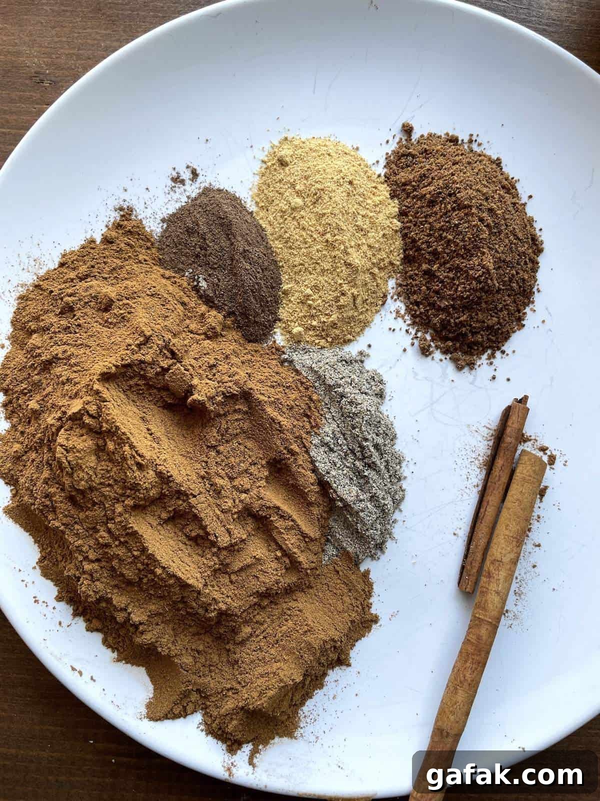A white plate with cinnamon, cardamom, ginger, allspice, cinnamon sticks, and nutmeg on it.