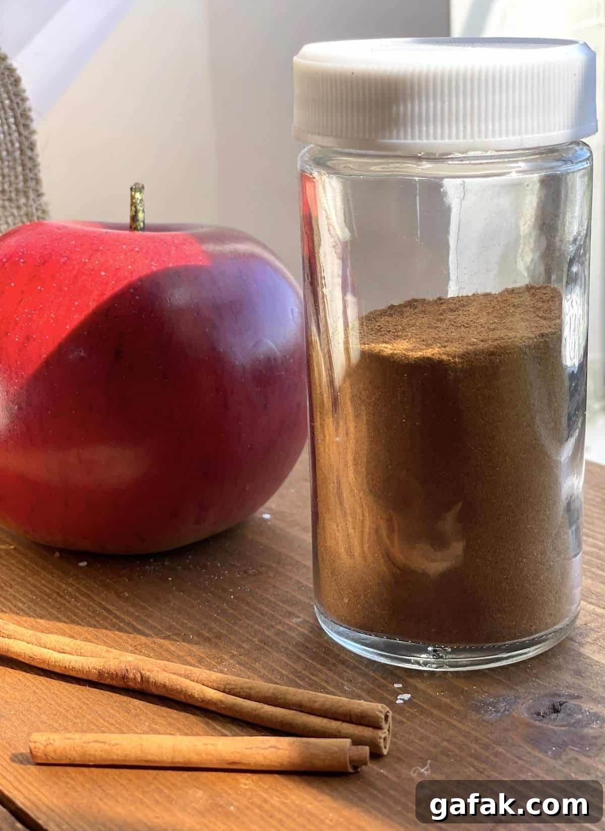 A jar of apple pie spice mix with an apple and cinnamon sticks.