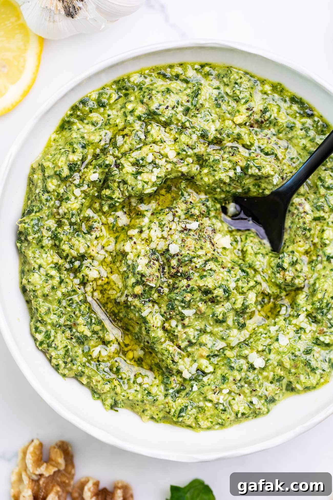 A close up look at a bowl of basil walnut pesto with a black spoon in the center.