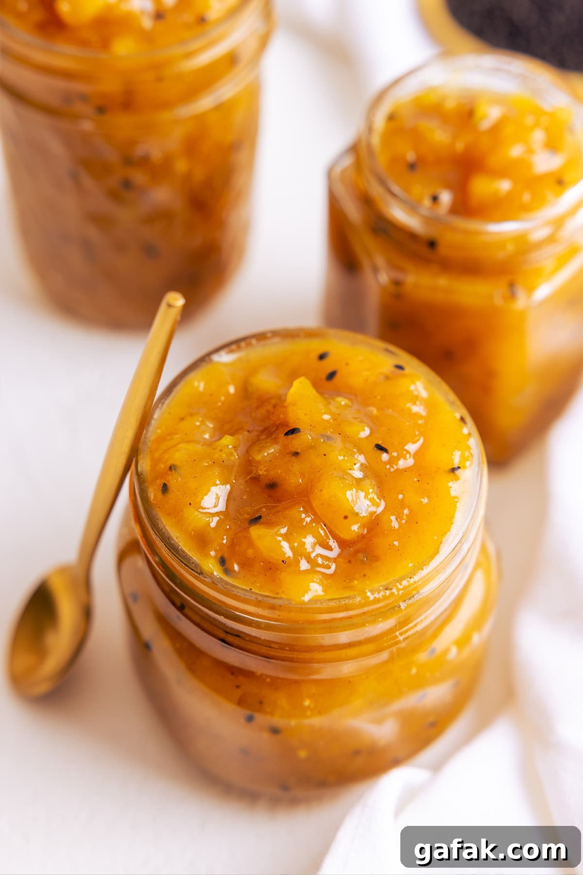 Close up picture of mango chutney in a glass jar with a brass spoon stood up next to the jar.