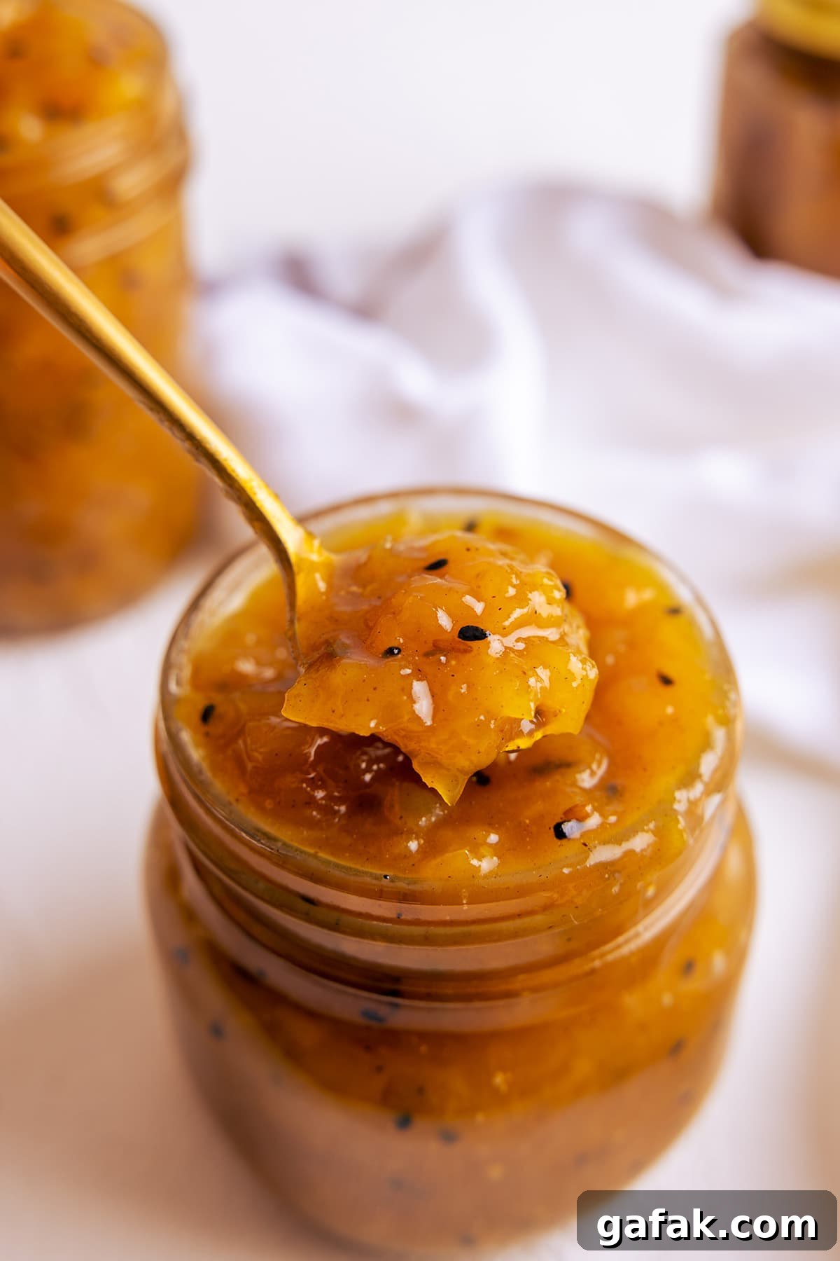 A brass spoon taking a spoon full of mango chutney out of a glass jar.