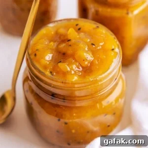 A jar full to the brim of mango chutney with a brass coloured spoon leaning up against the jar.