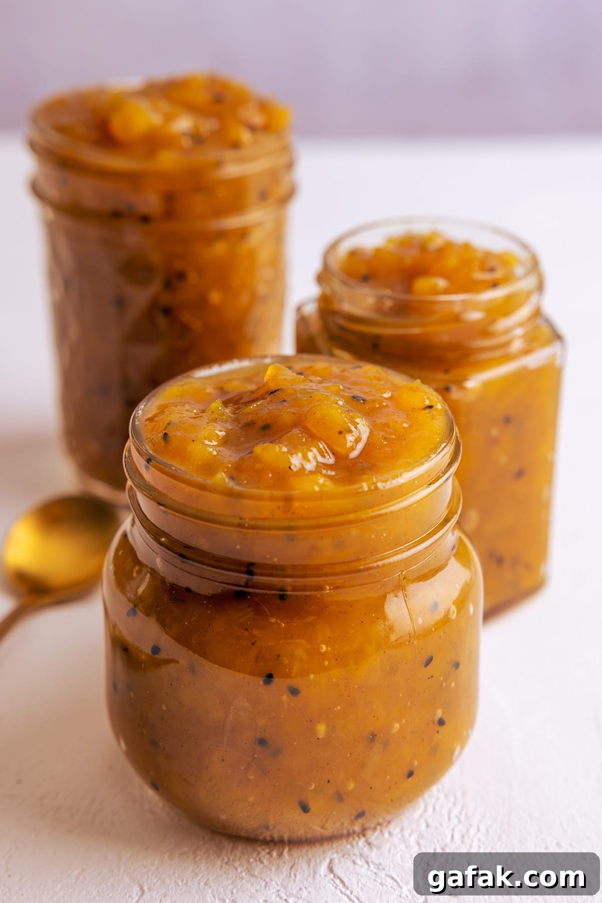 3 jars full of homemade mango chutney sat on a white board.