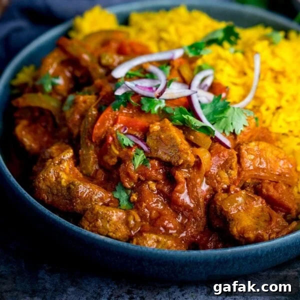Close up image of chicken Jalfrezi with pilau rice in a blue bowl