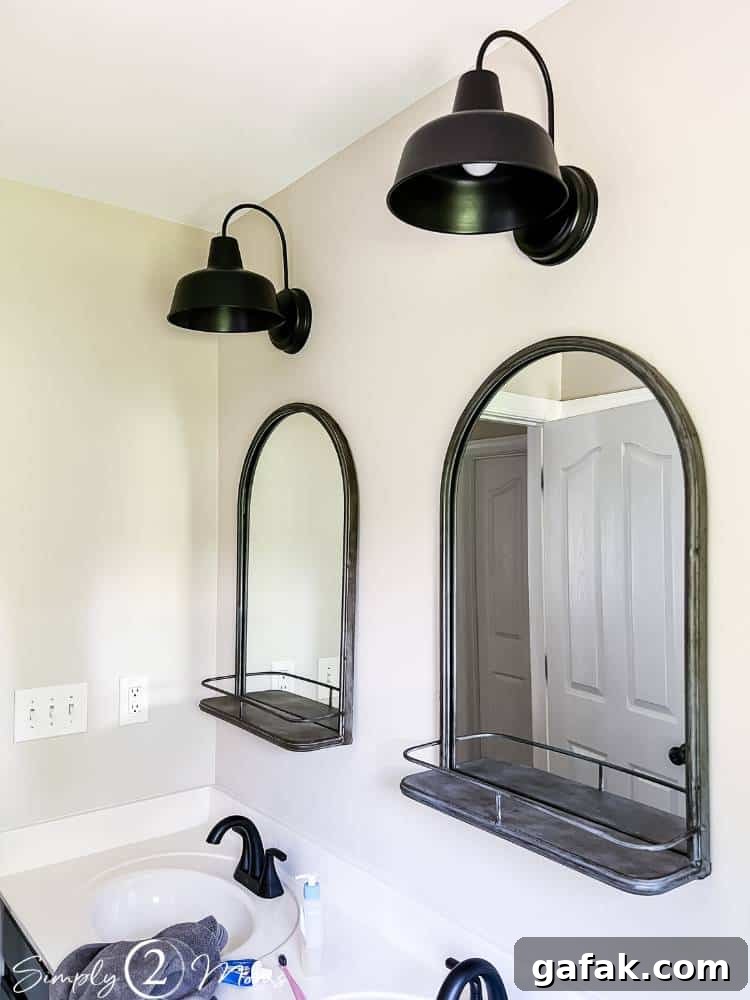 two mirrors with shelves with lights hung over them on wall above double bathroom sink vanity