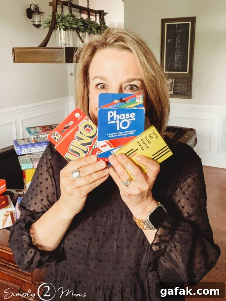 Anne from Simply2Moms holding decks of cards to play Uno, Phase10, and Taco Cat Goat Cheese Pizza.
