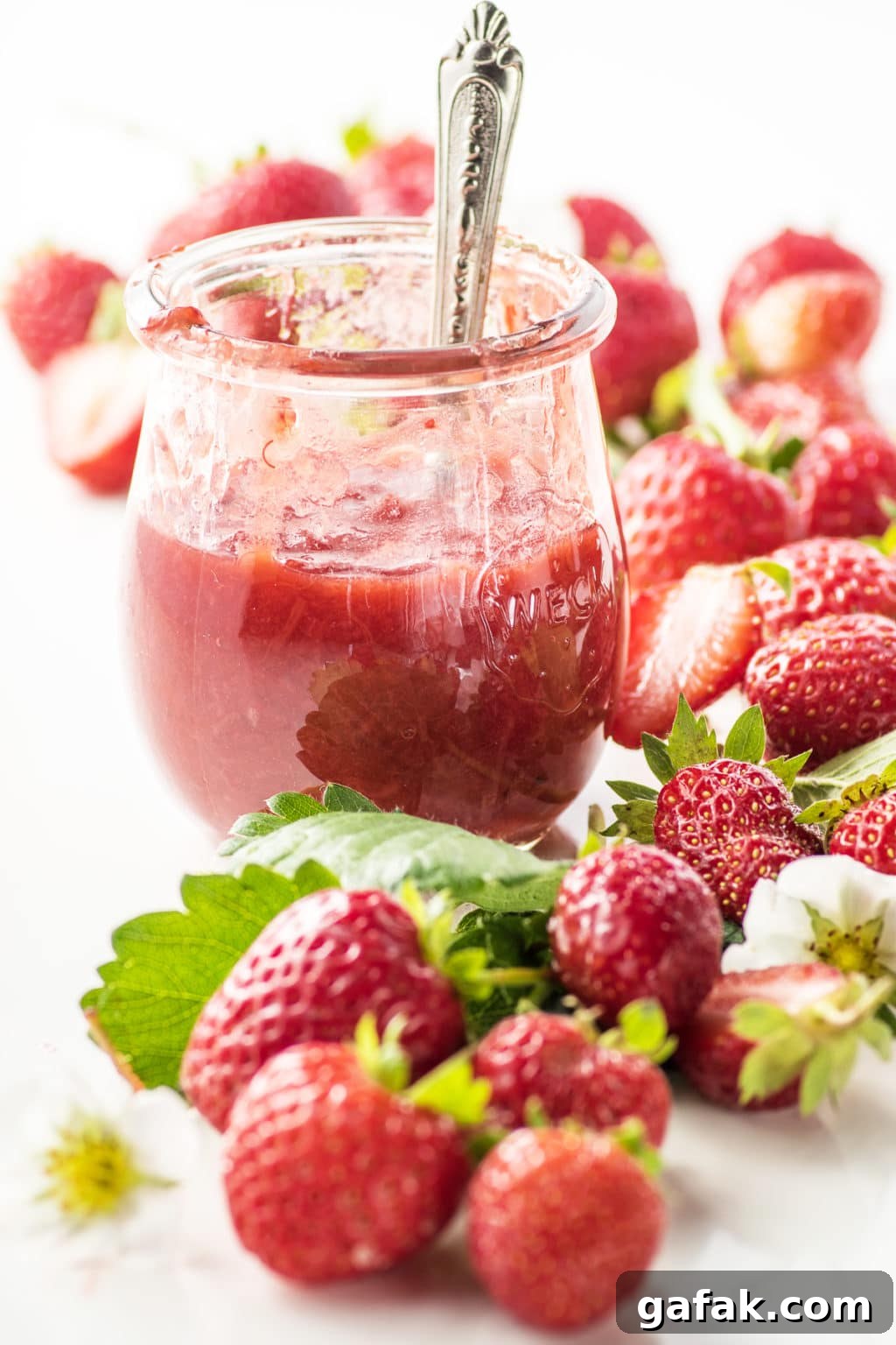 A jar of sugar free strawberry jam, with fresh strawberries piled around it.
