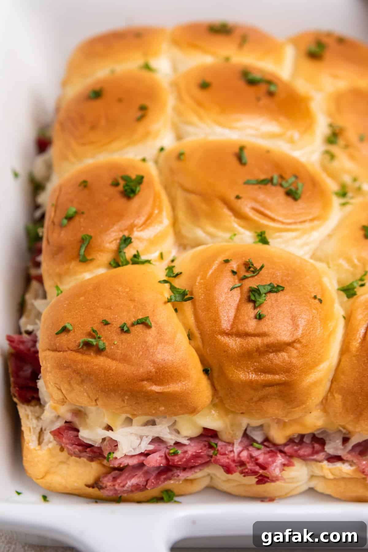 Classic Reuben Sliders with Melted Swiss and Tangy Thousand Island 2 Slow cooker reuben sliders in white pan with chopped parsley on top.