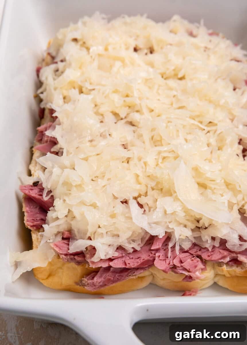 Classic Reuben Sliders with Melted Swiss and Tangy Thousand Island 7 Sauerkraut on top of corned beef and rolls in white baking dish.