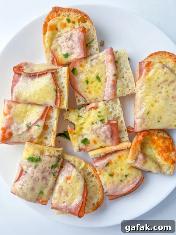 Slices of bread topped with ham, melted cheese, and chopped herbs are arranged on a white plate.