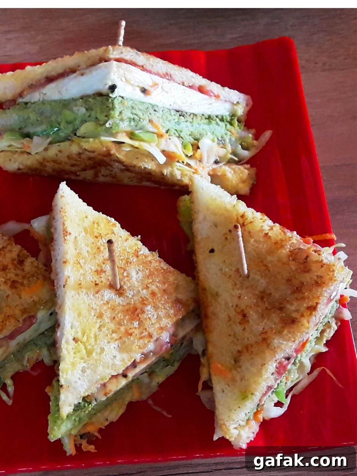 close-up of 3 vegetable club sandwich served on a red color plate.