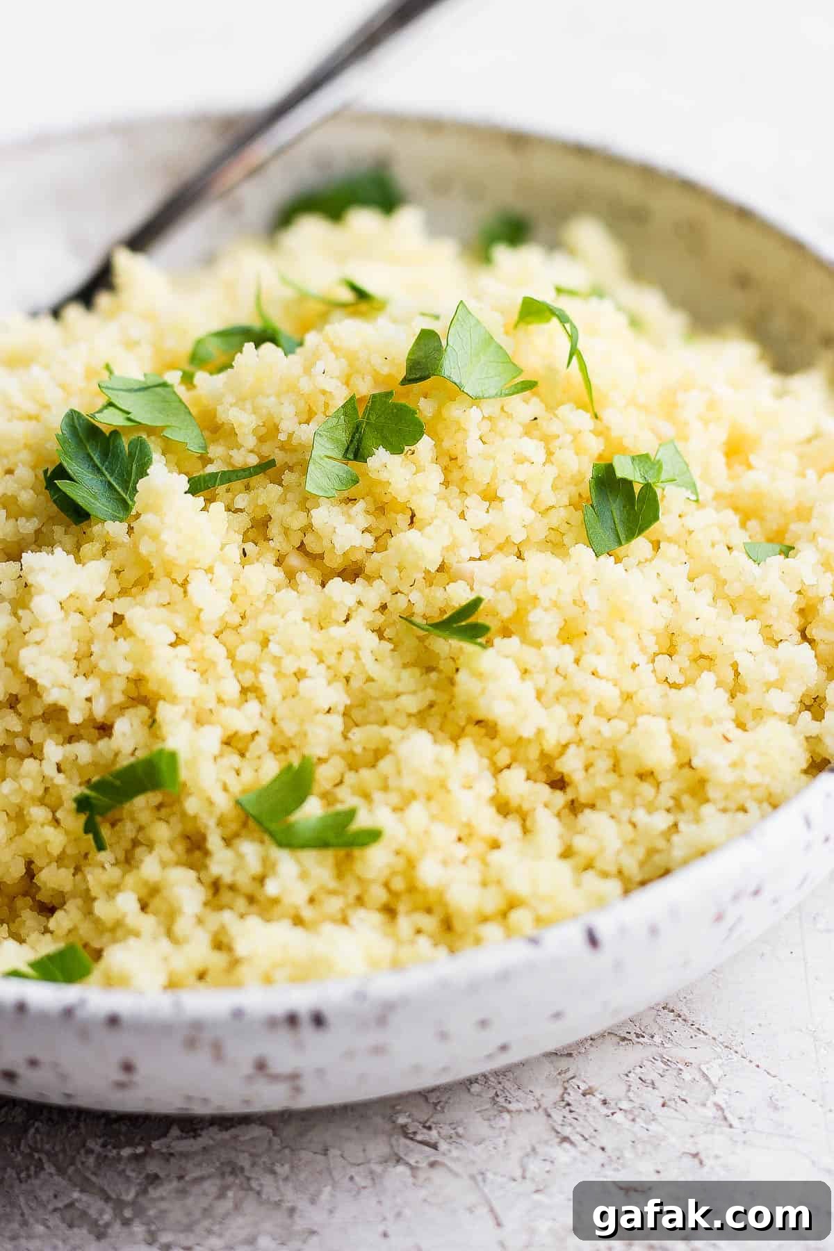 A bowl of cooked lemon couscous sprinkled with chopped parsley in a bowl.