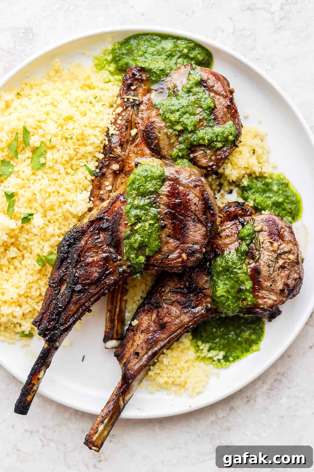 A plate with lemon couscous and three lamb chops topped with mint chimichurri.