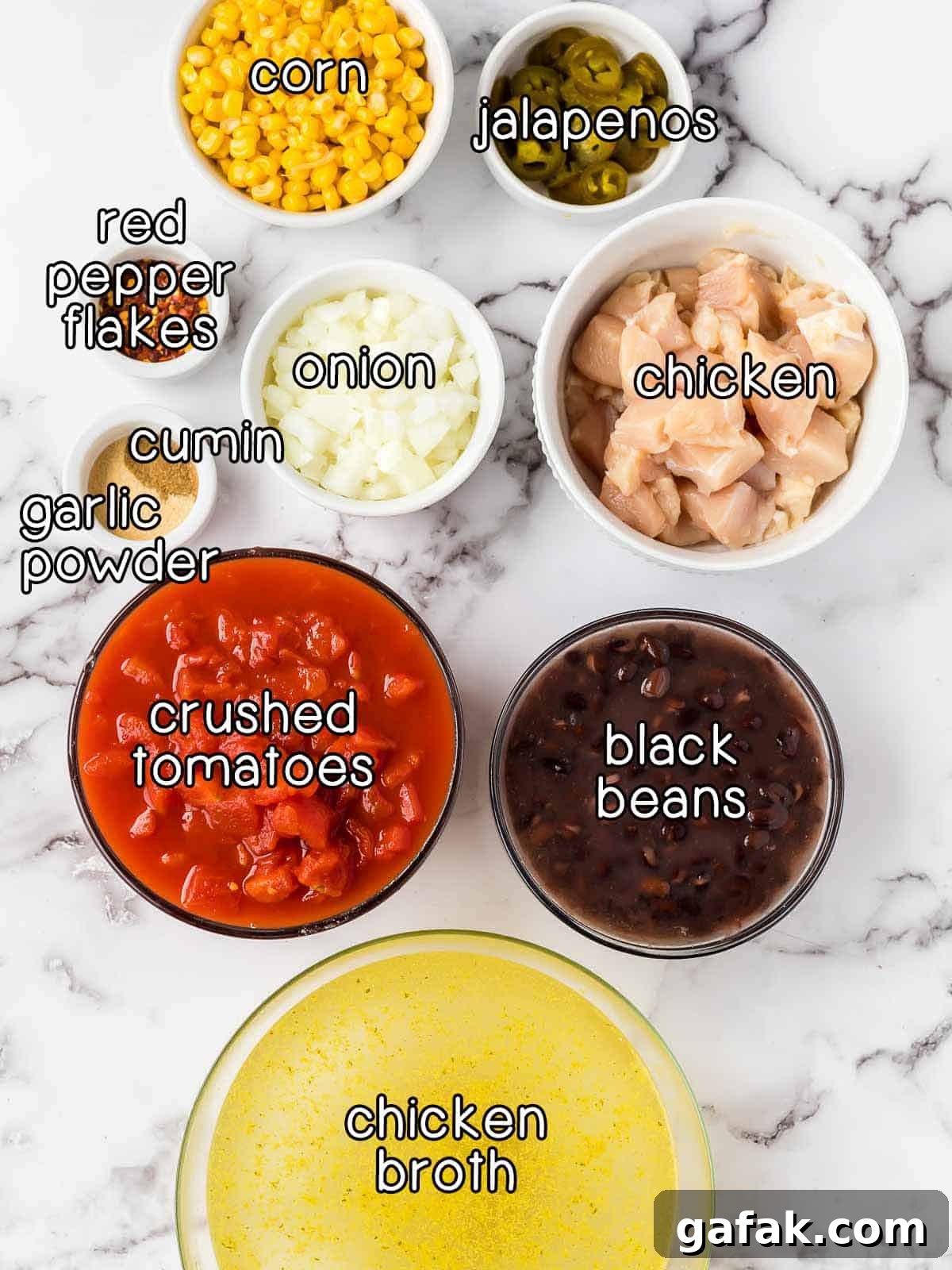 Overhead shot of ingredients - corn, jalapeños, onion, chicken, black beans, crushed tomatoes, chicken broth, red pepper flakes, cumin, and garlic powder.
