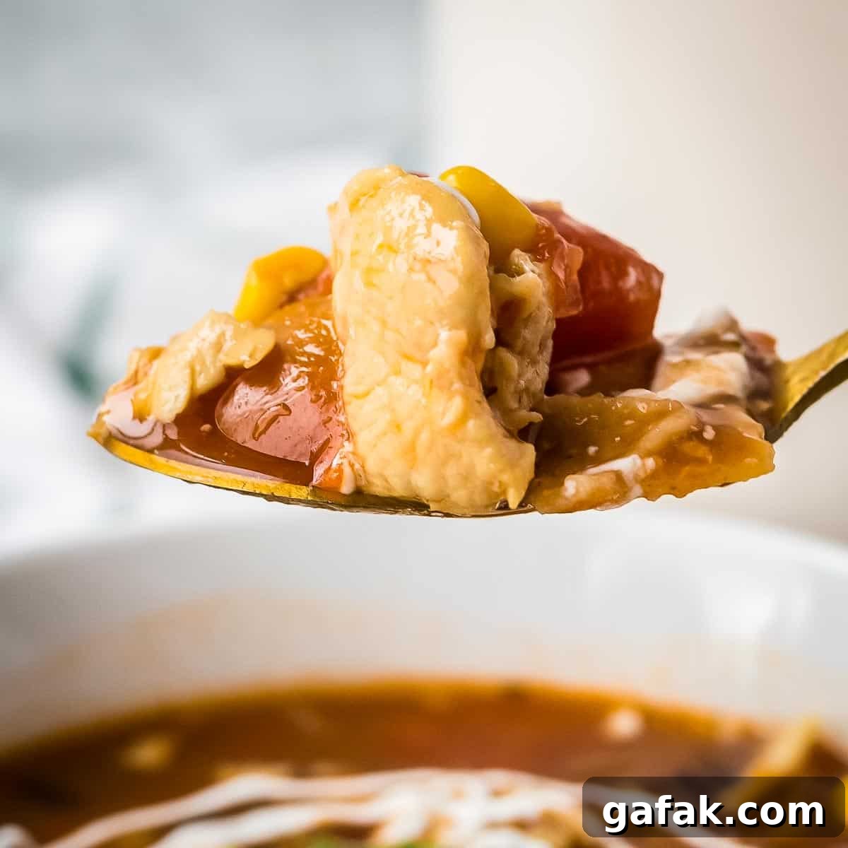 Side shot of a golden spoon holding a scoop of chicken tortilla soup over a white bowl full of it.