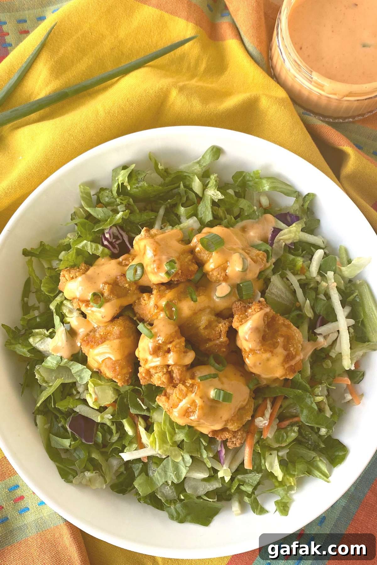 Chicken nuggets covered with homemade bang bang sauce on top of salad greens.