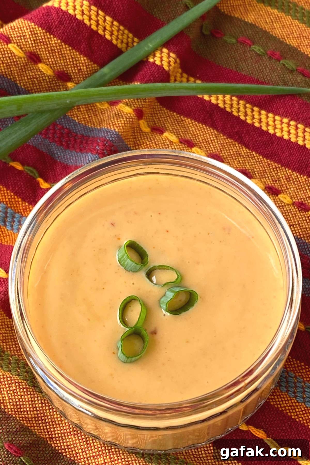 Easy bang, bang sauce in container garnished with green onion slices with more spring onion behind it.