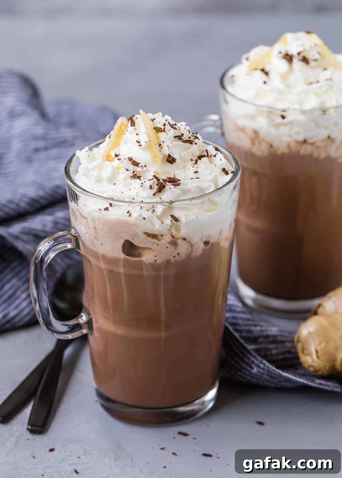 Hot cocoa in mugs, two black spoons, and a nob of fresh ginger.