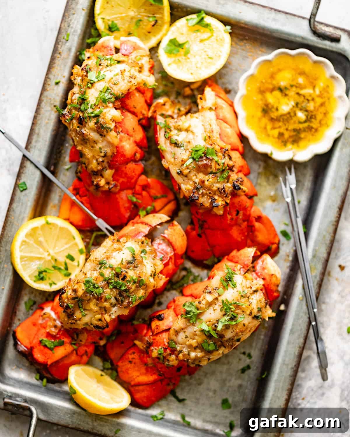 baked lobster tails on a serving dish with garlic butter brushed on top and lemon wedges on the side.