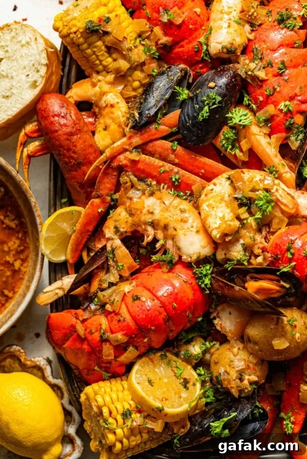 cajun seafood boil recipe on a large serving tray next to a bowl of seafood boil sauce, bread, and sliced lemons