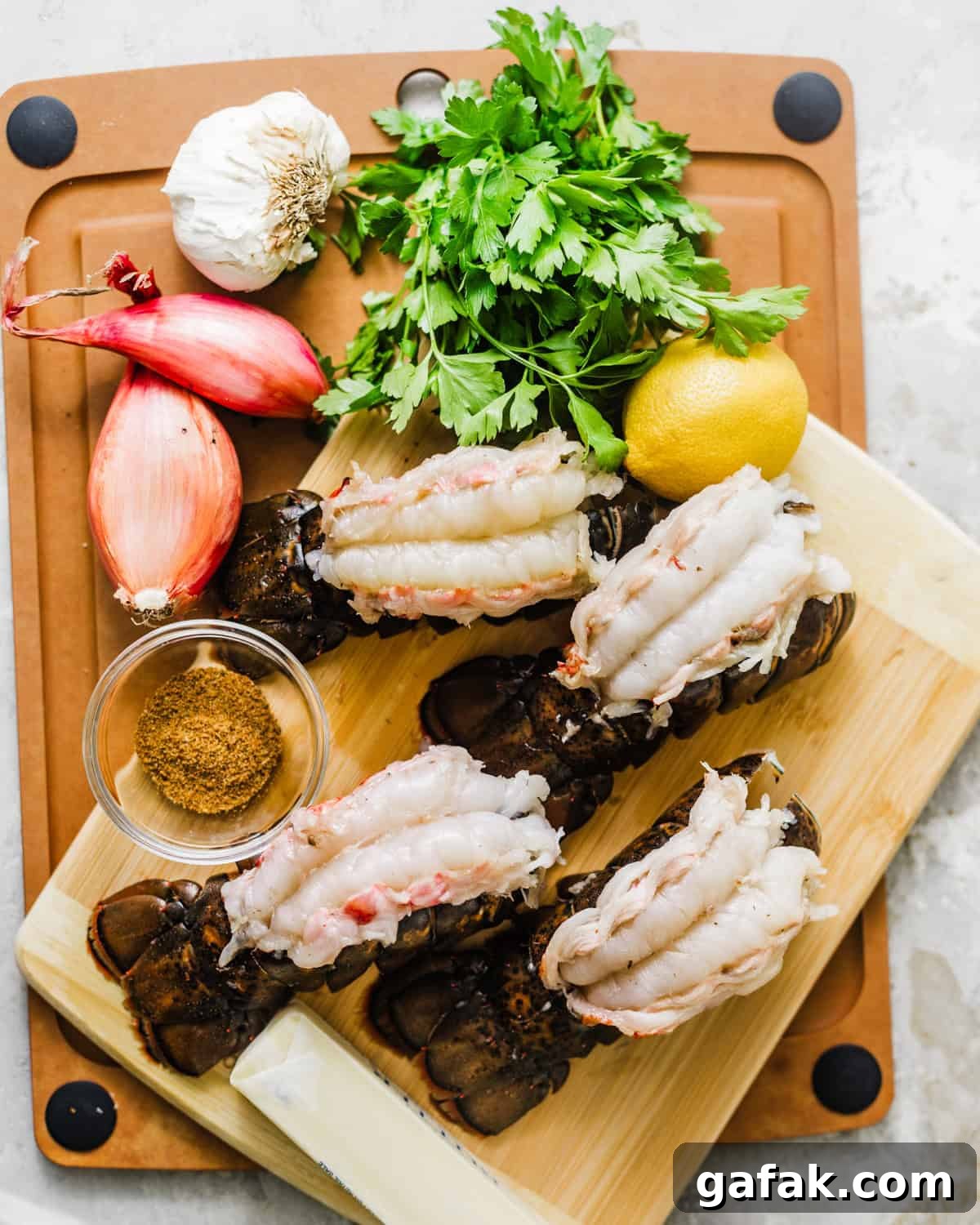 ingredients to make baked lobster tails - lobster, butter, shallots, garlic, parsley, lemon, garlic powder, and old bay seasoning.