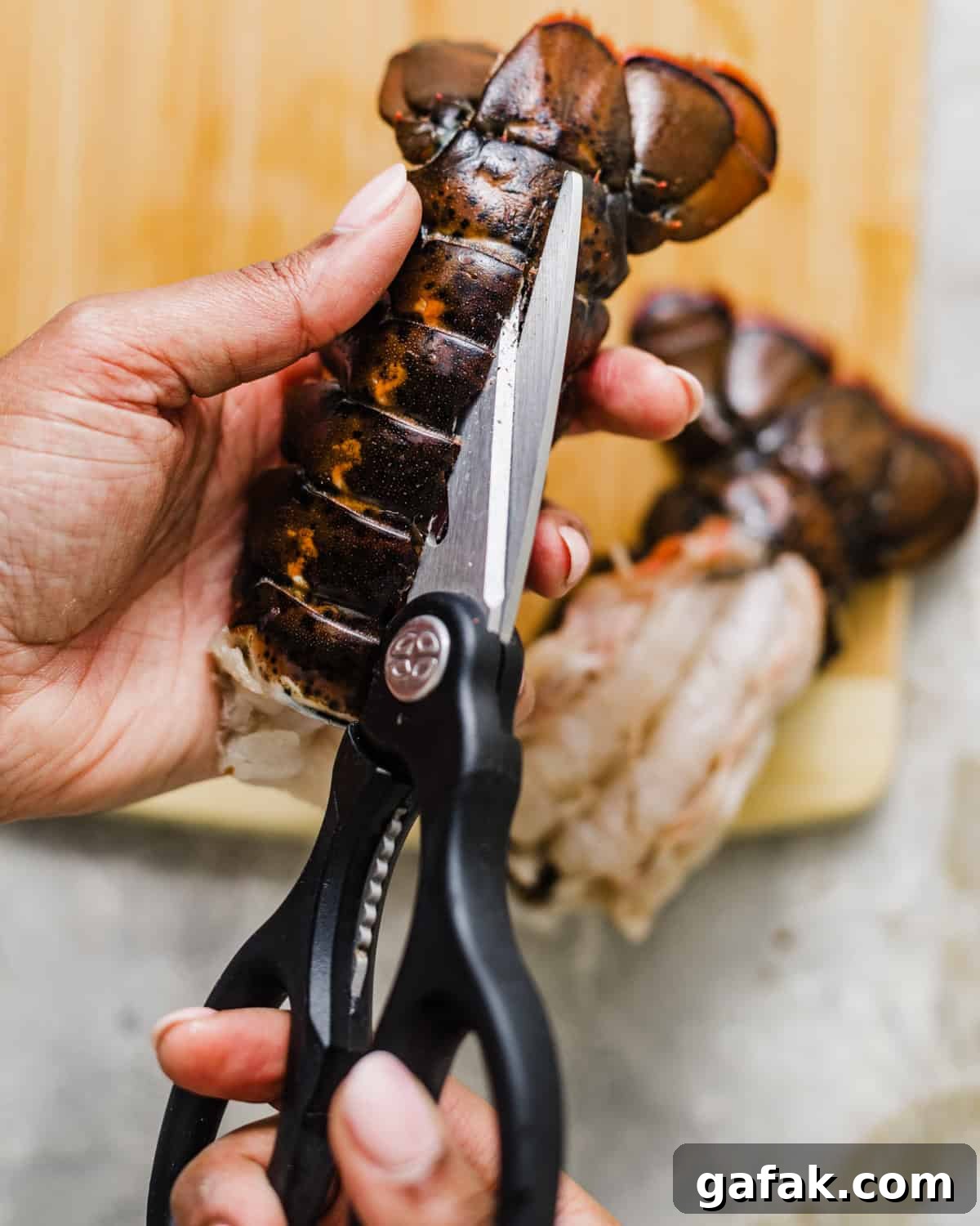 a hand holding kitchen shears cutting down the center of a lobster tail to butterfly the lobster.