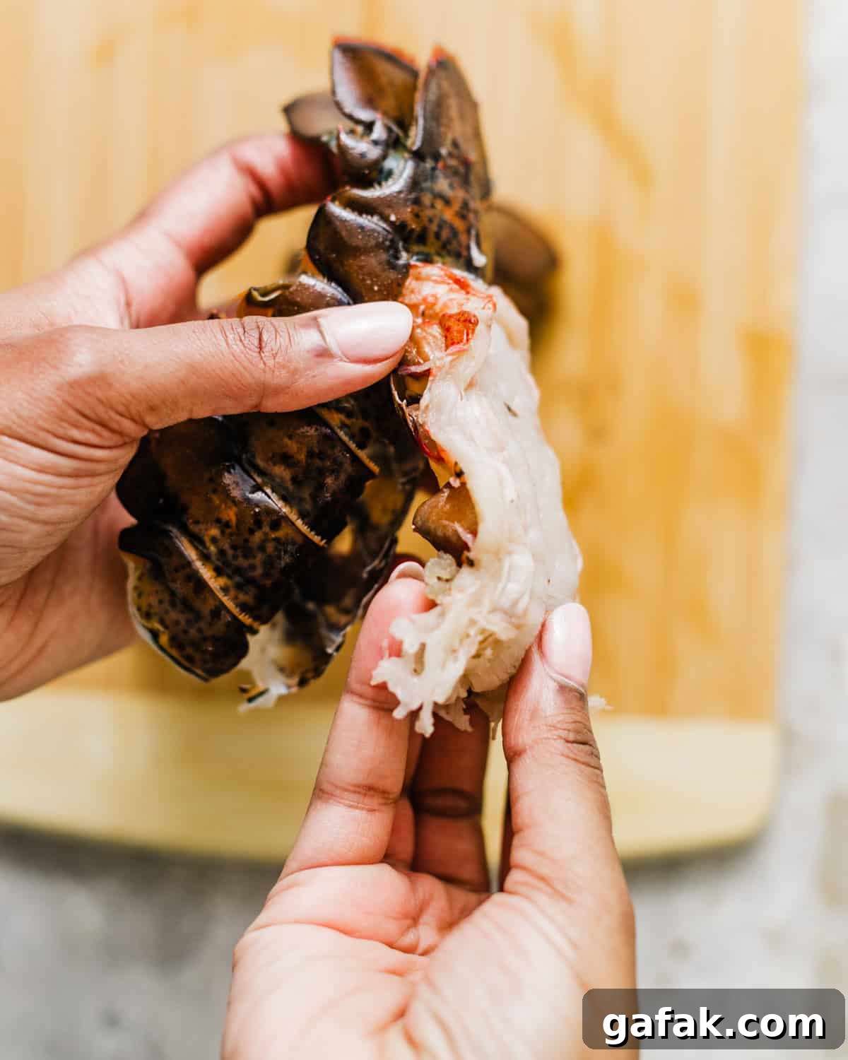 a hand pulling the lobster meat away from the lobster shell but keeping the bottom attached.