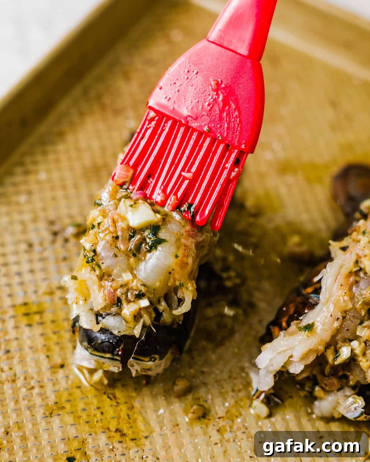 a pastry brush brushing the lobster tails with garlic butter before baking. 