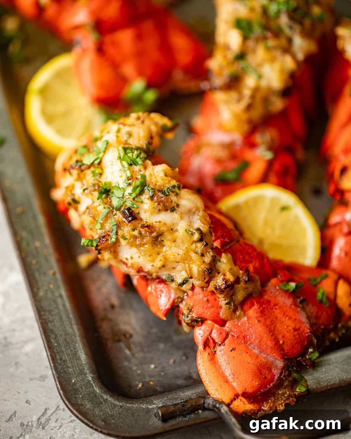 lobster tails on a serving tray with sliced lemons and additional garlic butter on top. 
