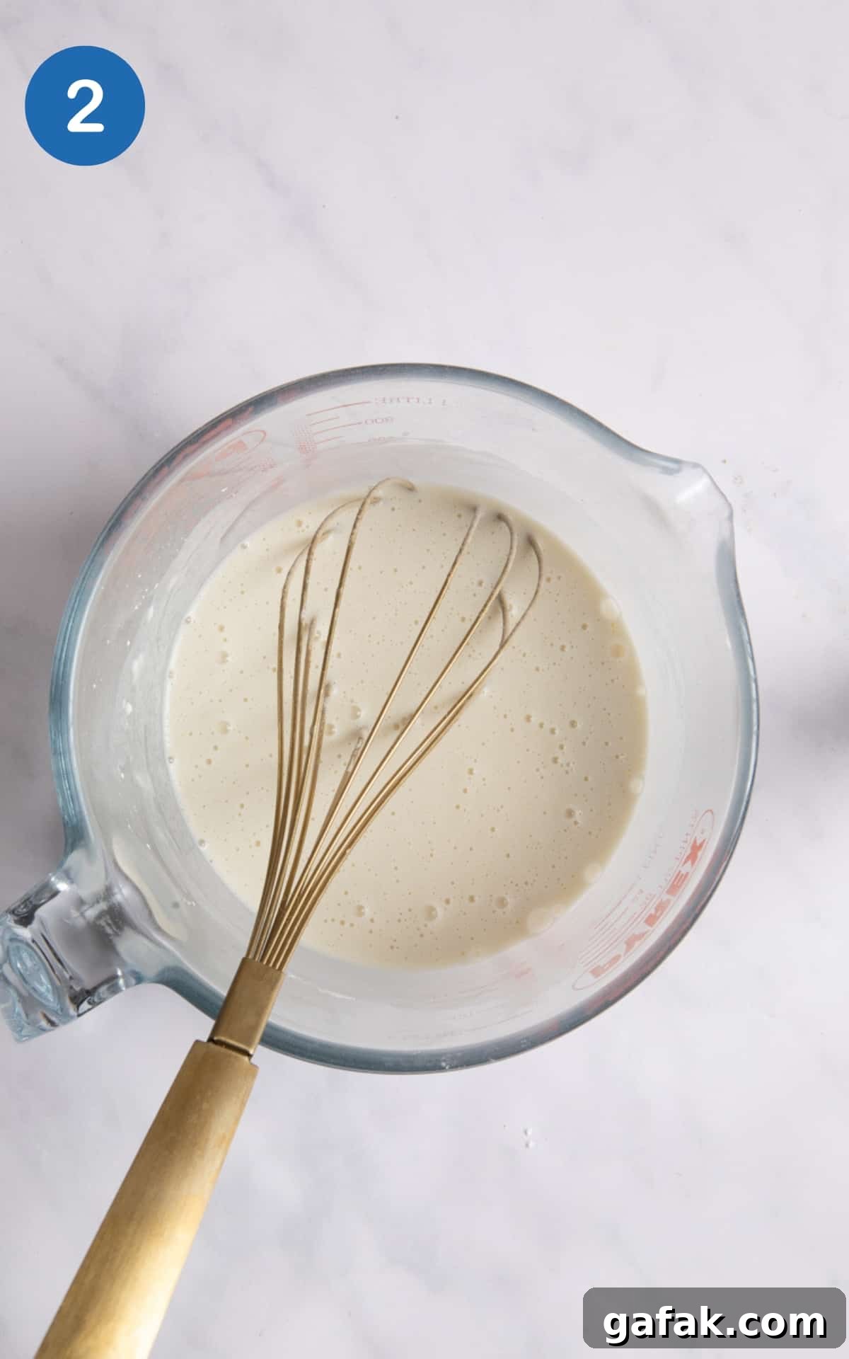 batter for Yorkshire puddings in large measuring jug with whisk in it. Measuring jug is on white background.