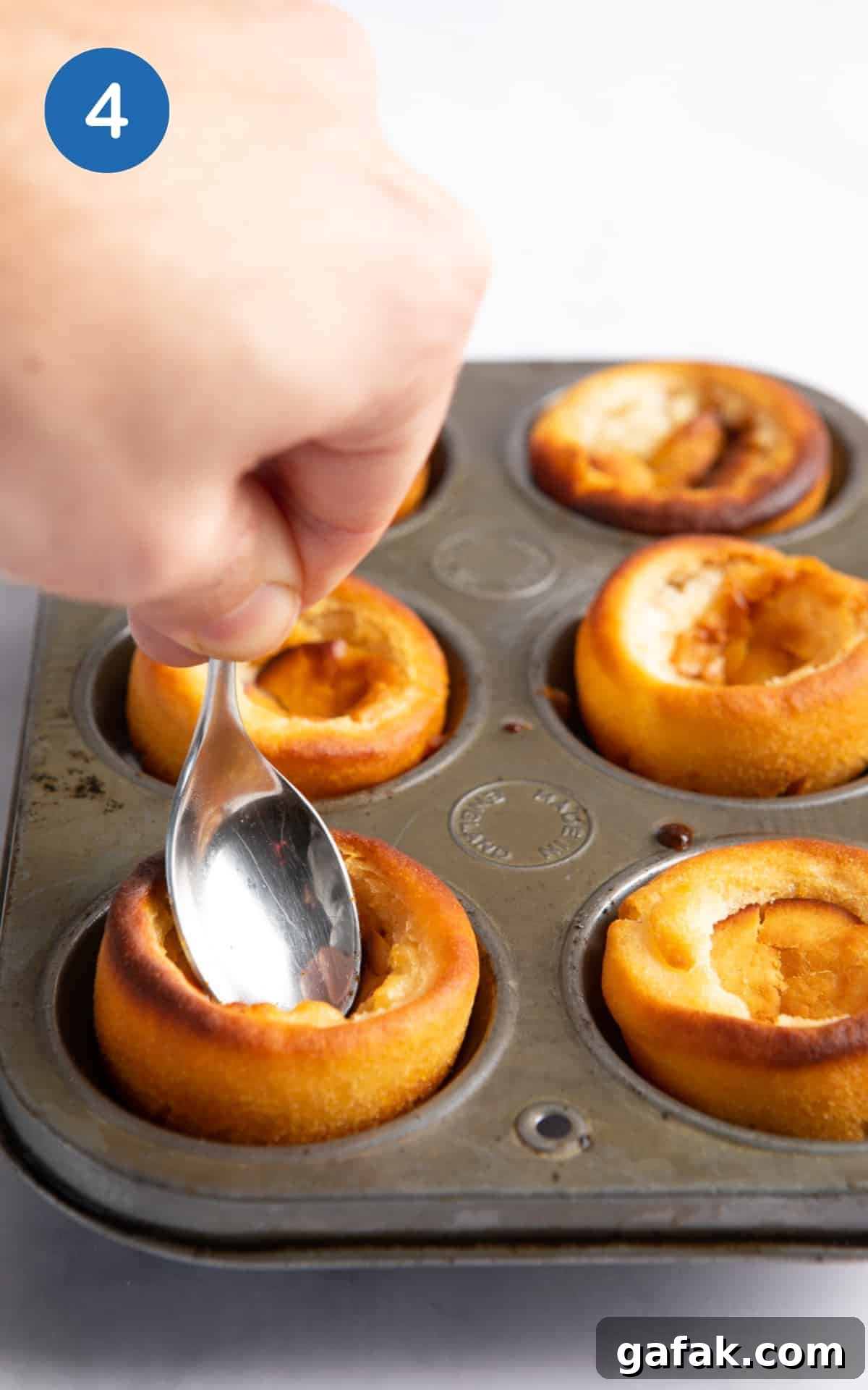 spoon being pressed into the centre of cooked Yorkshire puddings.