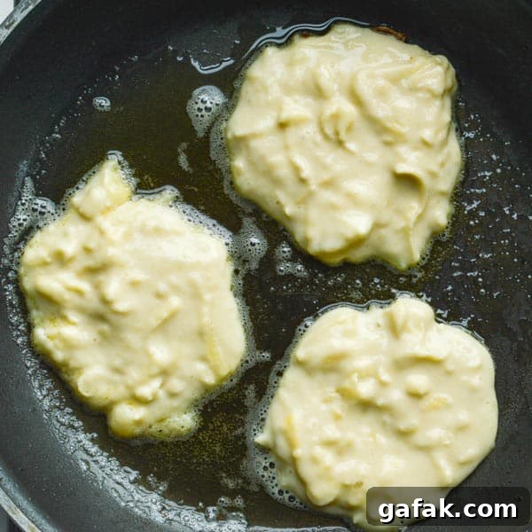 Three dollops of lumpy pale yellow batter in a frying pan