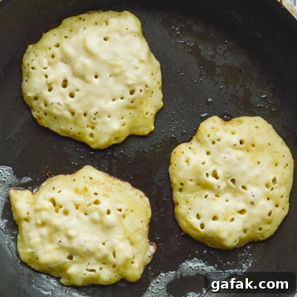 Three potato cakes half-cooked through in a black frying pan