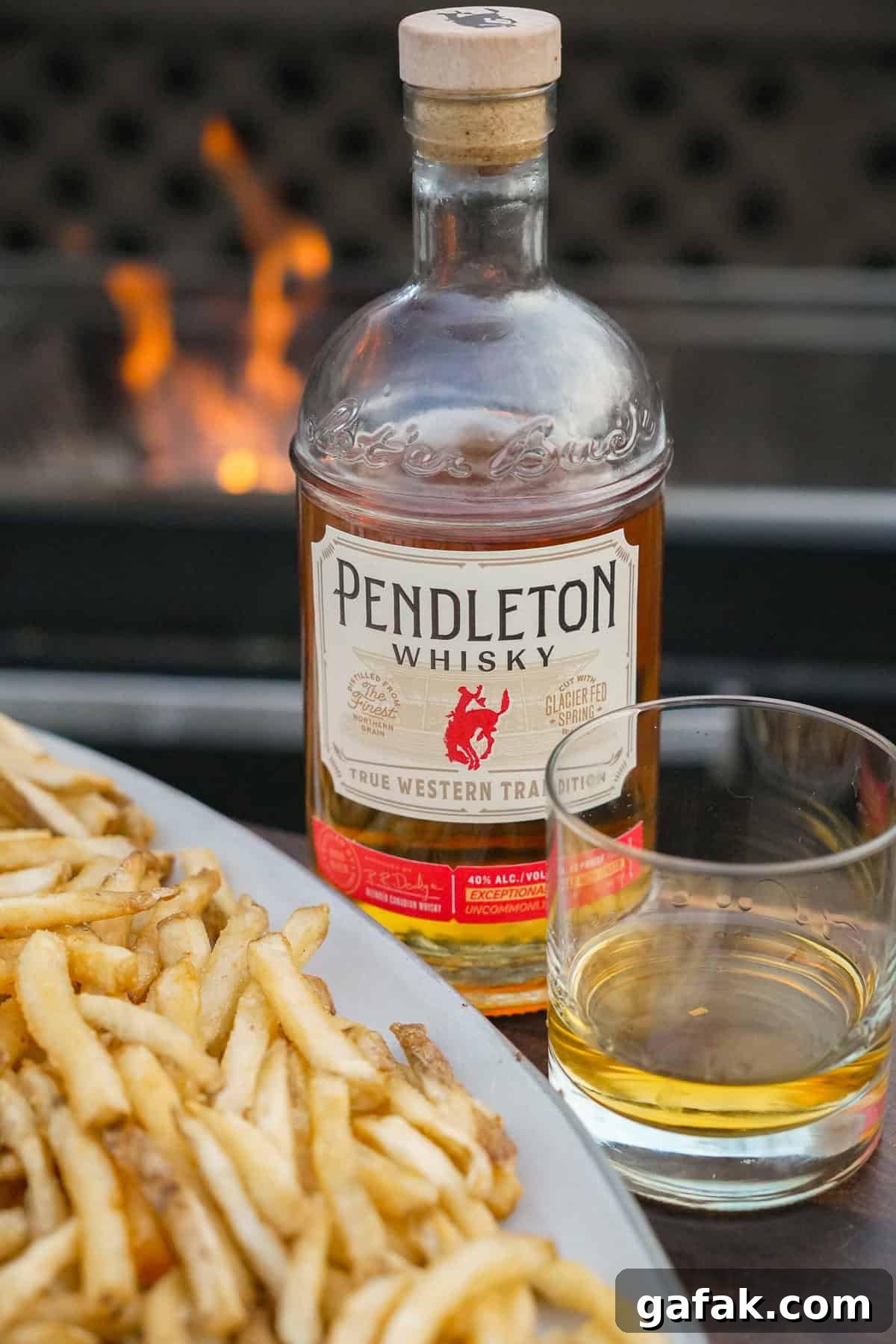A close up of Pendleton Whisky bottle and glass next to the plate of fries. 