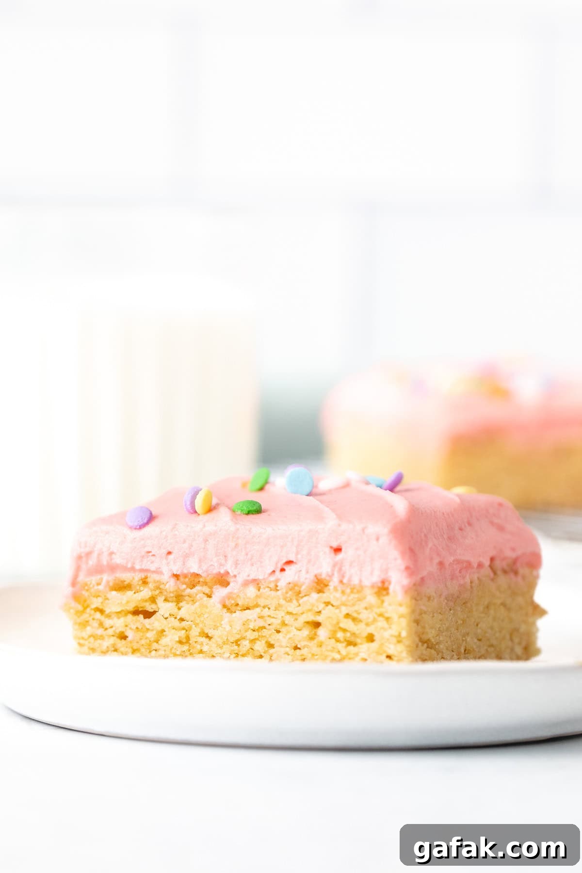 Frosted sugar cookie bars on plate with glass of milk