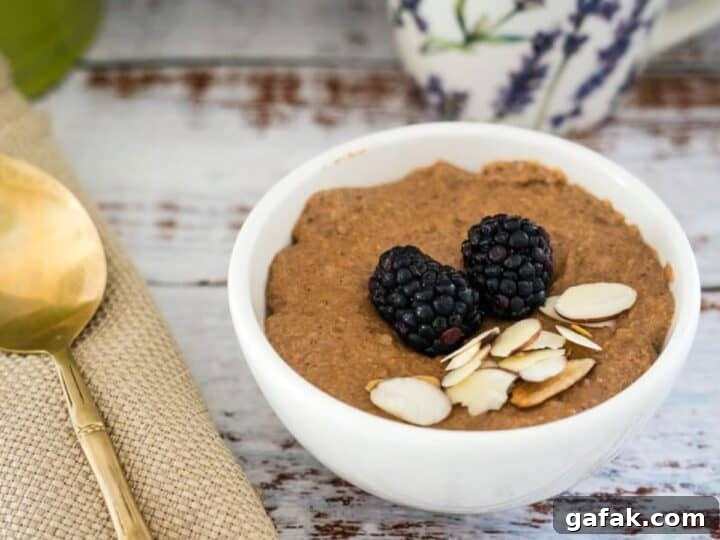 A bowl of almond-topped oatmeal garnished with blackberries, accompanied by a spoon on a cloth napkin.