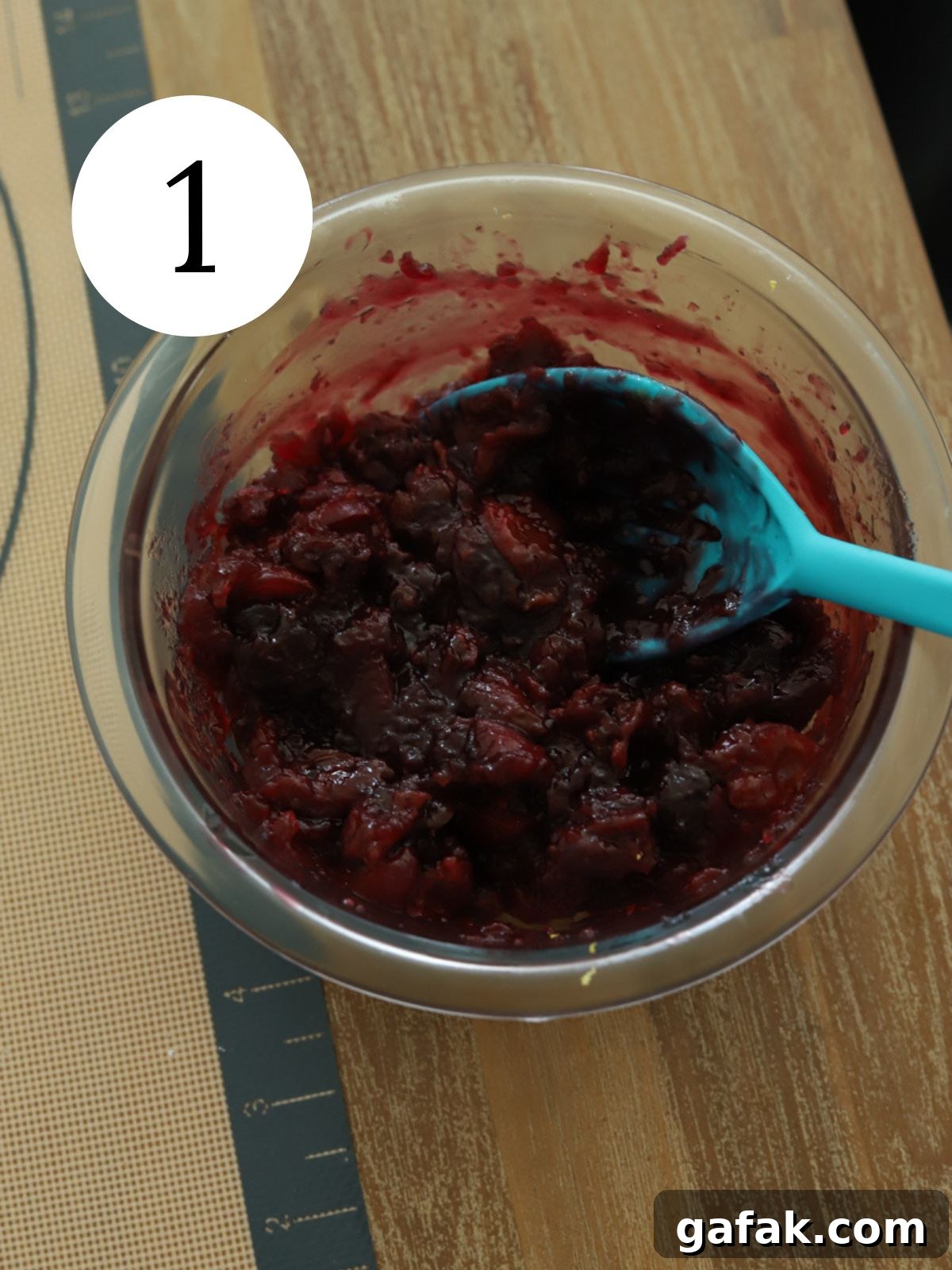 A glass bowl with cherry sauce and a blue spoon. 