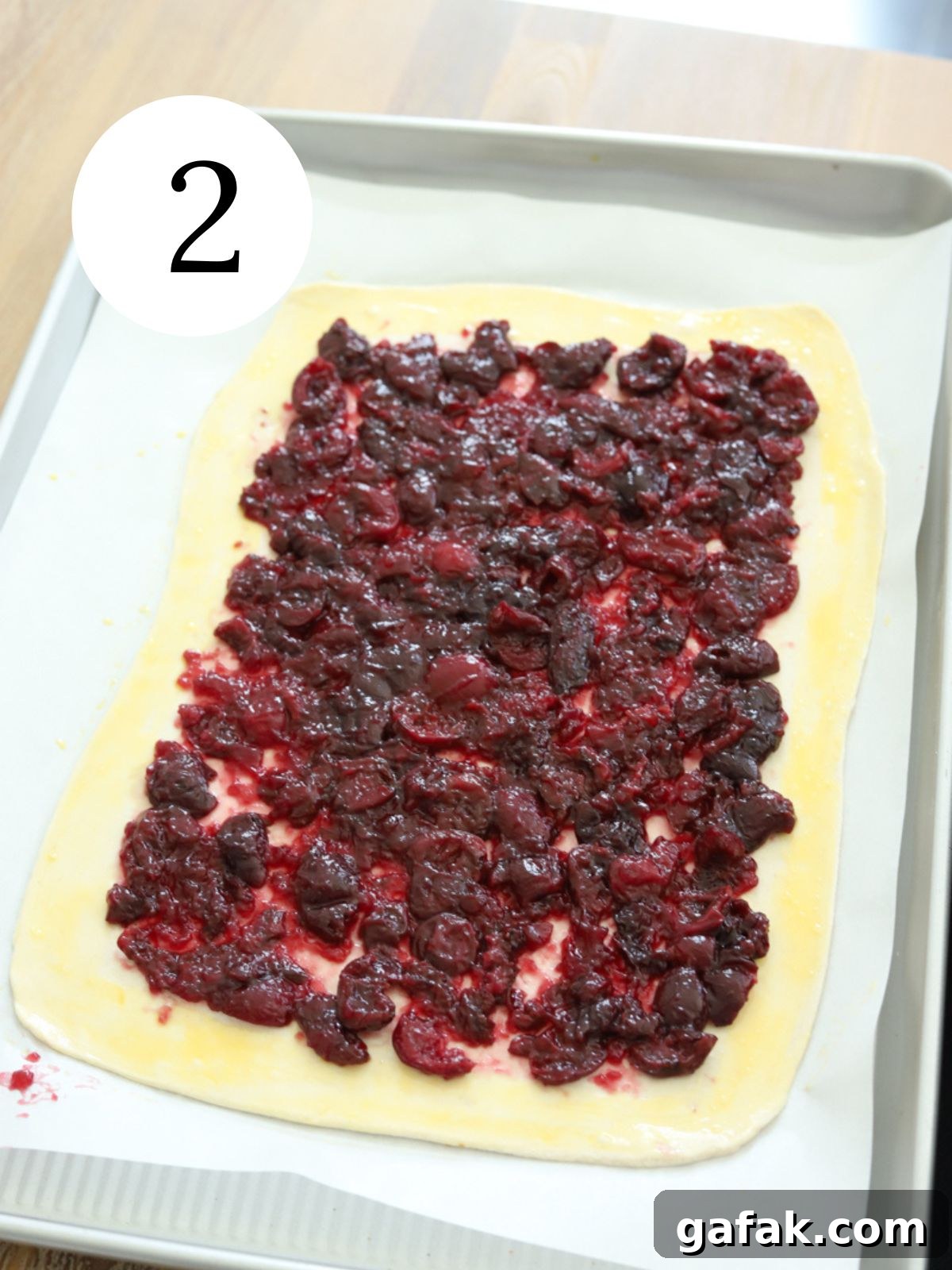 A rectangular pie crust on a baking sheet with cherry sauce spread on it. 