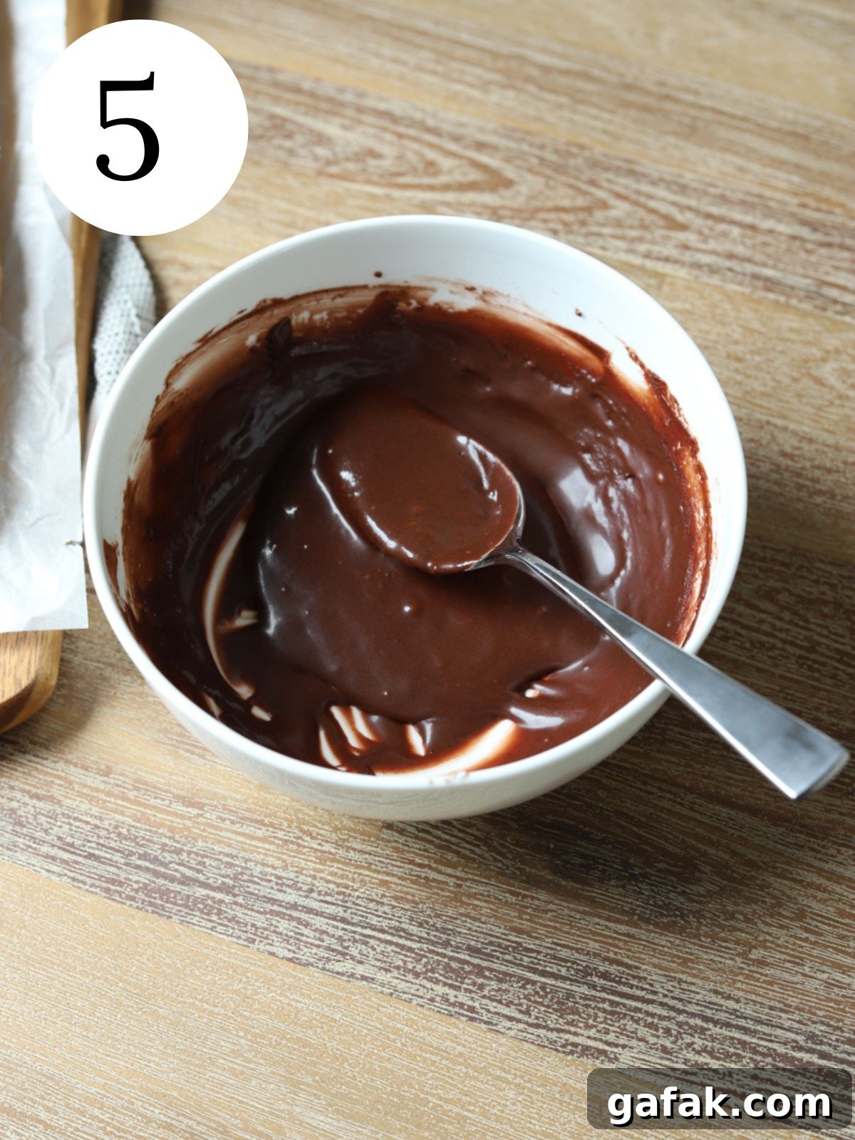 A white bowl with chocolate sauce and a spoon. 