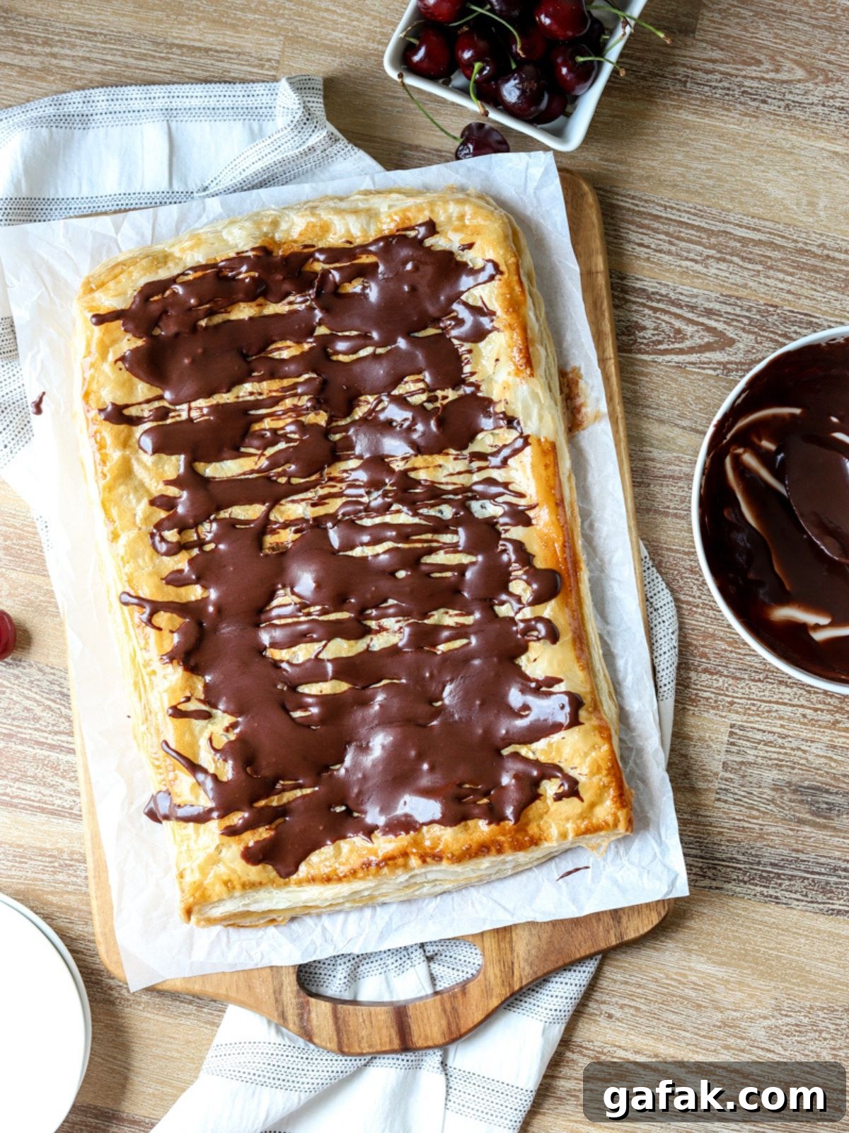 A giant slab pie on parchment paper and a bowl of cherries. 