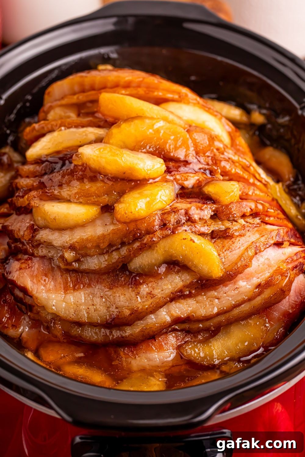 red slow cooker on table with a glazed apple spiral ham on table 